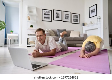 Healthy Mature Couple Watching Online Live Tv Yoga Fitness Class Tutorial Exercising At Home. Happy Old Middle Aged Husband And Wife Using Laptop Doing Virtual Training Workout Together In Apartment.