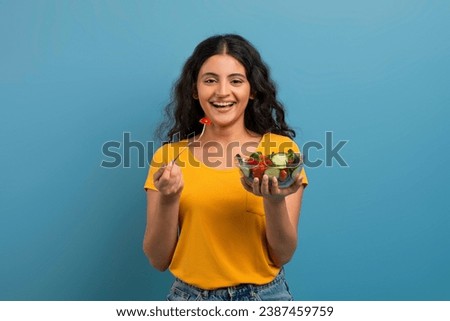 Healthy Meal. Portrait Of Happy Casual Indian Woman Eating Tasty Fresh Vegetable Salad, Holding Plate Bowl And Fork Looking At Camera. Satisfied Young Lady Isolated On Blue Background