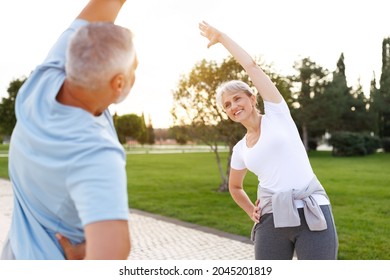 Healthy Mind And Body. Full Length Shot Of Happy Smiling Mature Family Man And Woman In Sportswear Stretching Arms While Warming Up Together Outdoors In Park On Sunny Morning. Active Lifestyle