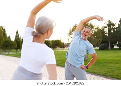 Healthy Mind And Body. Full Length Shot Of Happy Smiling Mature Family Man And Woman In Sportswear Stretching Arms While Warming Up Together Outdoors In Park On Sunny Morning. Active Lifestyle