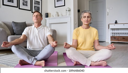 Healthy Mindful Old Mature Senior 60s Couple Meditating Together At Home. Calm Serene Older Middle Aged Family Do Yoga Breathing Exercise With Eyes Closed Feeling Stress Relief, Life Balance Concept.