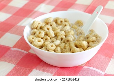 Healthy Morning Oat Cereal. Cheerios In Bowl Of Milk With Spoon. Low Sugar And High Fibre Breakfast. Isolated On Red And White Square Patterned Tablecloth.