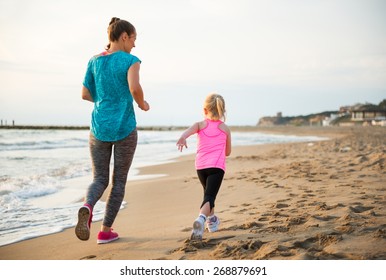 Healthy Mother And Baby Girl Running On Beach. Rear View