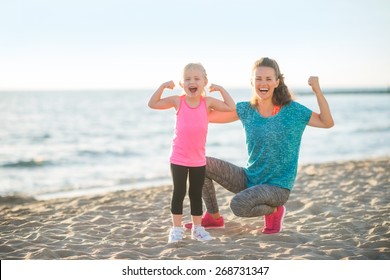 Healthy Mother And Baby Girl Showing Biceps On Beach