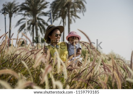 healthy mother and daughter playing and joking around while walking across the field full of pampas grass. photo taken during sunset with a vintage looking surroundings