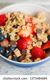 Healthy Muesli Breakfast Bowl With Granola Made Of Toasted Rolled Whole-grain Oats, Organic Honey, Milk Chocolate Chips And Graham Cracker Cookies Served With Fresh Strawberries And Huckleberries