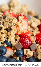 Healthy Muesli Or Cereal Breakfast Bowl With Granola Made Of Toasted Rolled Oats, Organic Honey, Milk Chocolate Chips And Tiny Graham Cracker Cookies Served With Fresh Strawberries And Blueberries