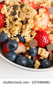 Healthy Muesli Or Cereal Breakfast Bowl With Granola Made Of Rolled Whole Grain Oats, Organic Honey, Milk Chocolate Chips And Tiny Graham Cracker Cookies Served With Fresh Strawberries And Blueberries