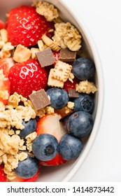 Healthy Muesli Or Cereal Breakfast Bowl With Granola Made Of Toasted Rolled Oats, Organic Honey, Milk Chocolate Chips And Tiny Graham Cracker Cookies Served With Fresh Strawberries And Blueberries