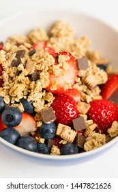 Healthy Muesli Or Cereal Breakfast Bowl With Granola Made Of Toasted Rolled Oats, Organic Honey, Milk Chocolate Chips And Tiny Graham Cracker Cookies Served With Fresh Strawberries And Blueberries