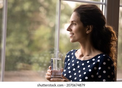 Healthy and natural. Side shot of pretty happy latin lady enjoy sunny day outside of window hold glass of clear mineral water. Young female take care of health beauty drink fresh pure aqua. Copy space