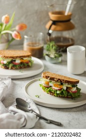 Healthy, natural spring breakfast or brunch. Serving of sandwiches with whole grain bread, avocado, eggs, radish, cucumber ion white plate with coffee and tulips on a white background - Shutterstock ID 2120202482