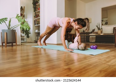 Healthy New Mom Working Out With Her Baby At Home. Yogi Mom Doing Push Up Exercises On An Exercise Mat. Young Mom Bonding With Her Baby During Her Post-natal Fitness Routine.