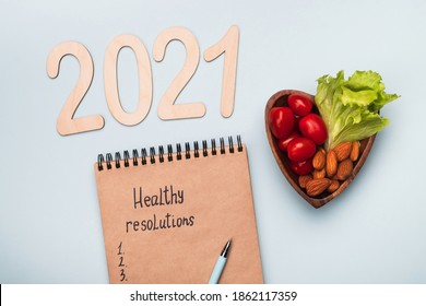 Healthy New Year Resolutions. Сoncept Of Healthy Eating, Diet And Sports In 2021. Notepad And Heart Shaped Plate With Vegetables And Nuts On Light Background. Top View