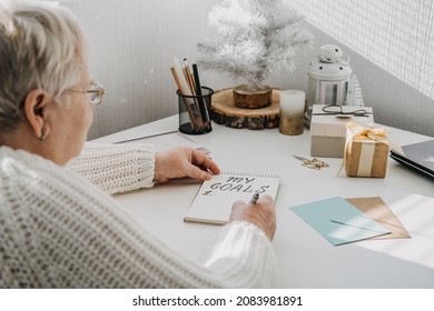 Healthy New Years Resolutions For Older Adults. Senior Mature Old Woman In White Sweater Writing Handwritten Text My Goals In Open Notepad On The Table. Planning And Setting Goals