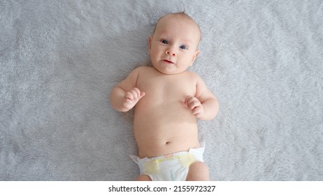 A Healthy Newborn Baby In A Nappy Without Clothes. Cute Baby With Blue Eyes . Happy Newborn Boy Lies On A Blue Blanket And Actively Moves His Arms And Legs. Half Full Length Body.