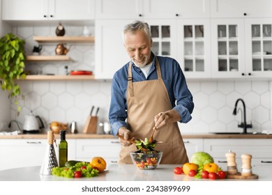 Healthy Nutrition Concept. Happy Senior Man Cooking Fresh Vegetable Salad In Kitchen, Smiling Elderly Gentleman In Apron Mixing Ingredients In Bowl While Preparing Tasty Meal At Home, Free Space - Powered by Shutterstock