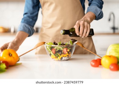 Healthy Nutrition Concept. Man Seasoning Vegetable Salad While Cooking In Kitchen, Unrecognizable Male Chef Wearing Apron Adding Olive Oil While Preparing Vegetarian Meal At Home, Cropped Shot - Powered by Shutterstock