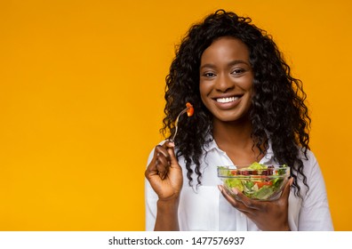 Healthy Nutrition. Happy African American Lady Eating Vegetable Salad, yellow studio background, copy space