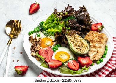 Healthy nutritious paleo keto breakfast diet Fried eggs, avocado, grilled chicken fillet, nuts, strawberries and fresh salad. Keto breakfast or lunch. top view,
