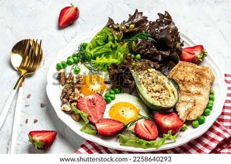 Healthy nutritious paleo keto breakfast diet Fried eggs, avocado, grilled chicken fillet, nuts, strawberries and fresh salad. Keto breakfast or lunch. top view,