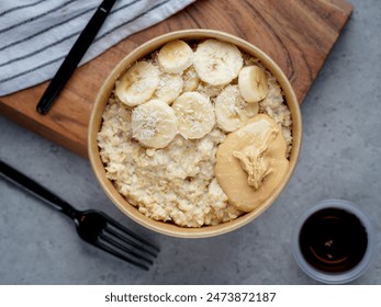 Healthy oatmeal bowl with bananas, peanut butter, and shredded coconut, served in an eco-friendly container on a gray surface, ideal for a nutritious and delicious breakfast - Powered by Shutterstock