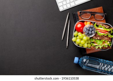 Healthy office lunch box with sandwich and fresh vegetables, water bottle, nuts and fruits on desk. Top view flat lay with copy space