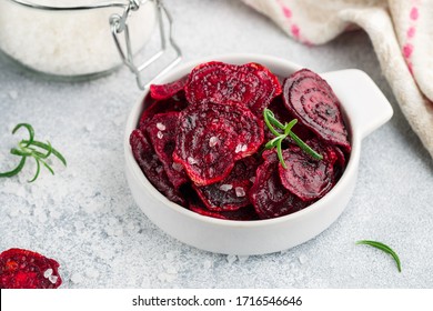 Healthy organic Purple Baked Beet (beetroot) Chips with olive oil, large Sea Salt and rosemary in a white bowl on a grey concrete background close up. Dietary useful snack. Selective focus - Powered by Shutterstock