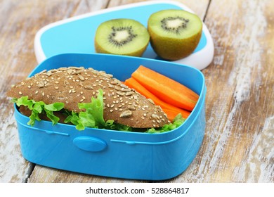Healthy Packed Lunch Box Containing Brown Cheese Sandwich, Crunchy Carrots And Kiwi Fruit
