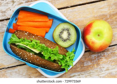 Healthy Packed Lunch Box Containing Brown Cheese Sandwich, Fresh Cut Carrots, Kiwi Fruit And Red Apple
