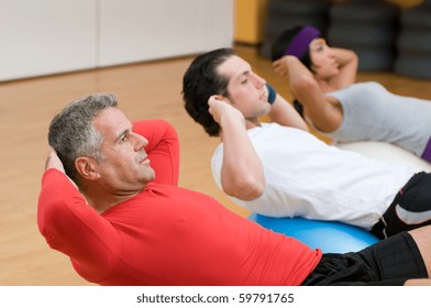 Healthy people with mature instructor doing sit-ups on fitness ball at gym - Powered by Shutterstock