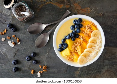 Healthy Pineapple, Mango Smoothie Bowl With Coconut, Bananas, Blueberries And Granola. Above View On A Dark Background.