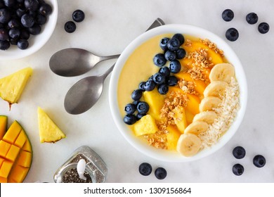 Healthy pineapple, mango smoothie bowl with coconut, bananas, blueberries and granola. Top view scene on a bright background.