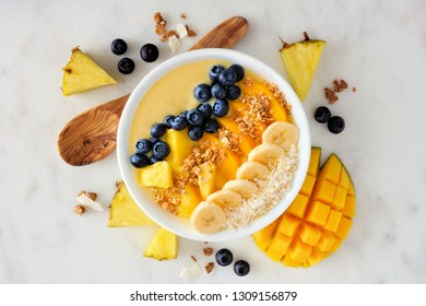 Healthy pineapple, mango smoothie bowl with coconut, bananas, blueberries and granola. Above view scene on a bright background. - Shutterstock ID 1309156879