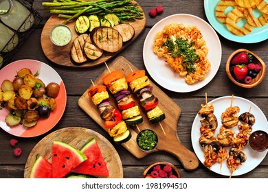 Healthy plant based summer bbq table scene. Top view on a dark wood background. Grilled fruit and vegetables, skewers, cauliflower steak and vegetarian sides. Meat substitute concept. - Shutterstock ID 1981994510