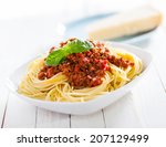 Healthy plate of Italian spaghetti topped with a tasty tomato and ground beef Bolognese sauce and fresh basil on a rustic white wooden table