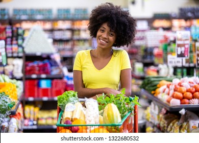 Healthy positive happy african woman holding a shopping cart full of fruit and vegetables.