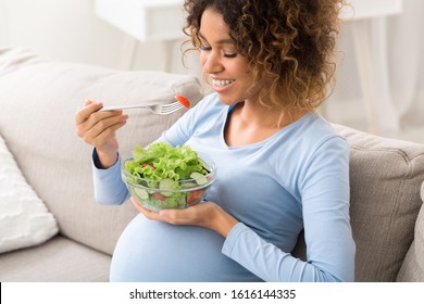 Healthy pregnancy food. African-american girl eating fresh vegetable salad, resting on sofa at home