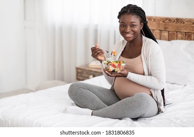 Healthy Pregnancy Nutrition. Happy Pregnant African American Woman Eating Fresh Vegetable Salad While Sitting On Bed At Home, Holding Bowl With Tasty Organic Food And Smiling At Camera, Copy Space
