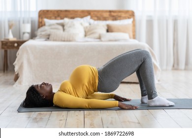 Healthy pregnant african american woman exercising on yoga mat at home, working on her hips, copy space. Black lady future mother taking care about her body and health, doing sport