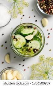 Healthy probiotic food. Homemade fermented cucumbers with garlic, dill and pepper in a glass jar. Light gray background. Top view, close-up, vertical orientation.
