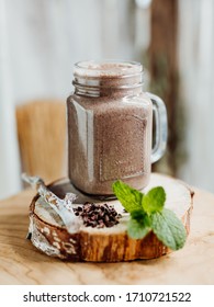 Healthy Protein Shake With Banana, Peanut Butter, Oats And Agave Syrup In A Stylish Glass, Decorated With Chocolate Protein, Oatmeal And Mint On A Wooden Plate, Brown, Beige, Bright