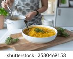 Healthy pumpkin soup with potatoes served by a woman with apron in the kitchen. Homemade food