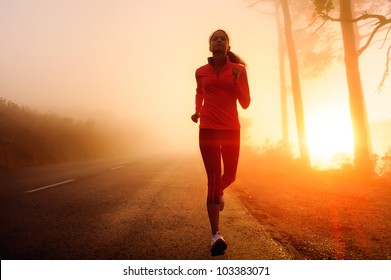 Healthy running runner woman early morning sunrise workout on misty mountain road workout jog. sunflare through the mist gives atmospheric feel and depth to these fitness images