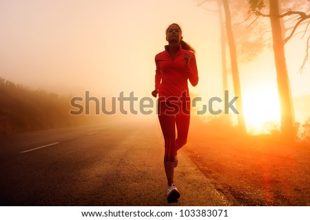 Healthy running runner woman early morning sunrise workout on misty mountain road workout jog. sunflare through the mist gives atmospheric feel and depth to these fitness images