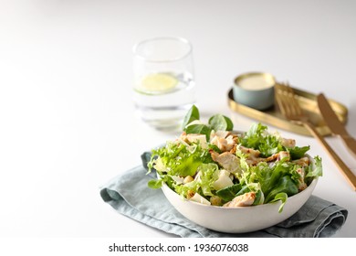 Healthy salad with  different lettuce, croutons,cheese,  chicken and dressing with especial sauce. Caesar salad in the white plate served with glass water and gold cutlery on the restaurant table.