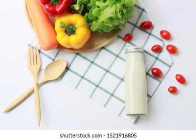 Healthy Salad With Glass Bottle Of Caesar Salad Dressing, Vegetables With Green Oak Lettuce, Bell Peppers, Carrot And Tomatoes And Spoon And Fork On White Background, Copy Space