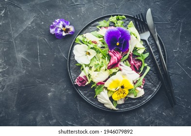 Healthy salad with green and purple lettuce and edible flowers on black background. Spring salad mix with edible flowers. Top view. Copy space. - Shutterstock ID 1946079892