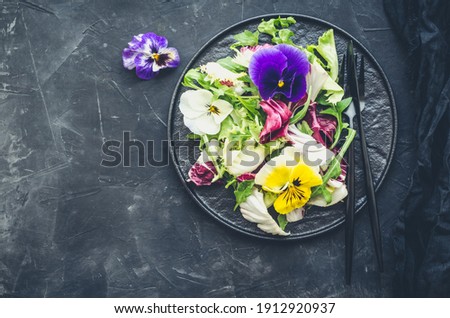 Healthy salad with green and purple lettuce and edible flowers on black background. Spring salad mix with edible flowers. Top view. Copy space.
