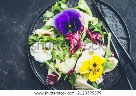 Healthy salad with green and purple lettuce and edible flowers on black background. Spring salad mix with edible flowers. Top view.